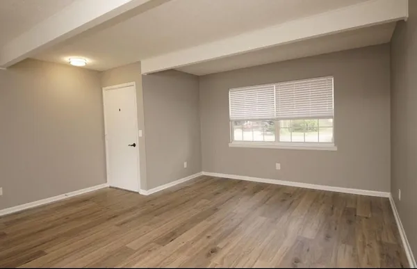 a view of an empty room with wooden floor and a window