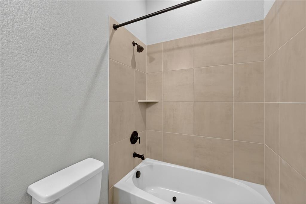 2237 Pika Road Northlake, TX 76247 - Photo 26 of 37 White bathtub with a built-in shelf, large-format beige wall tiles, and matte black fixtures