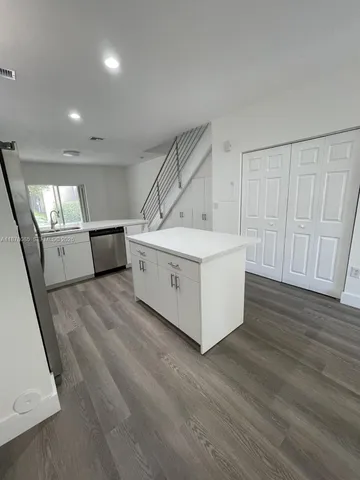 a view of an empty room with wooden floor and a kitchen