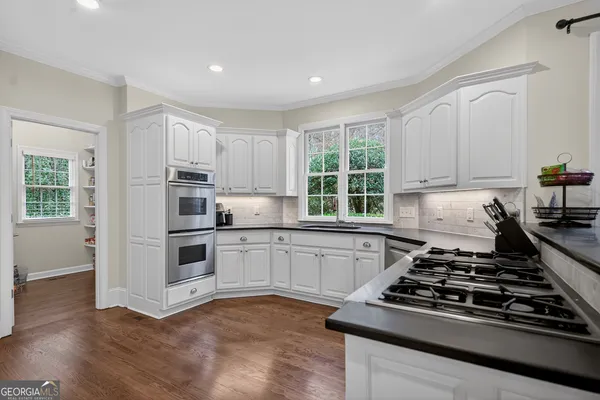 a kitchen with stainless steel appliances granite countertop a stove top oven a sink a dining table and chairs with wooden floor