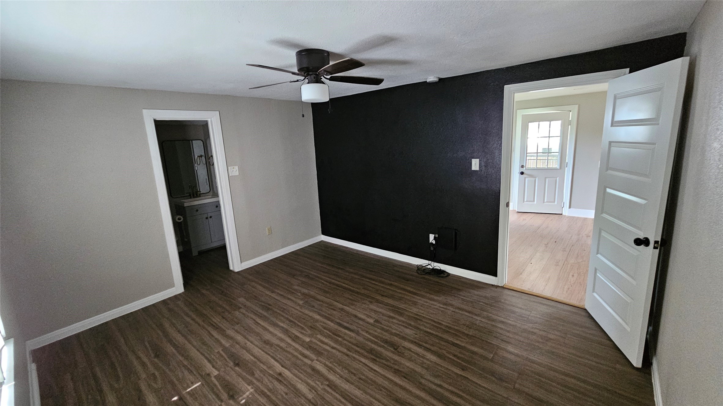 2415 Perry Street Baytown, TX 77521 - Photo 13 of 23 The primary bedroom features wood-look flooring, a ceiling fan, and a bold accent wall. It has a doorway leading to a bathroom and another to a bright adjoining room.