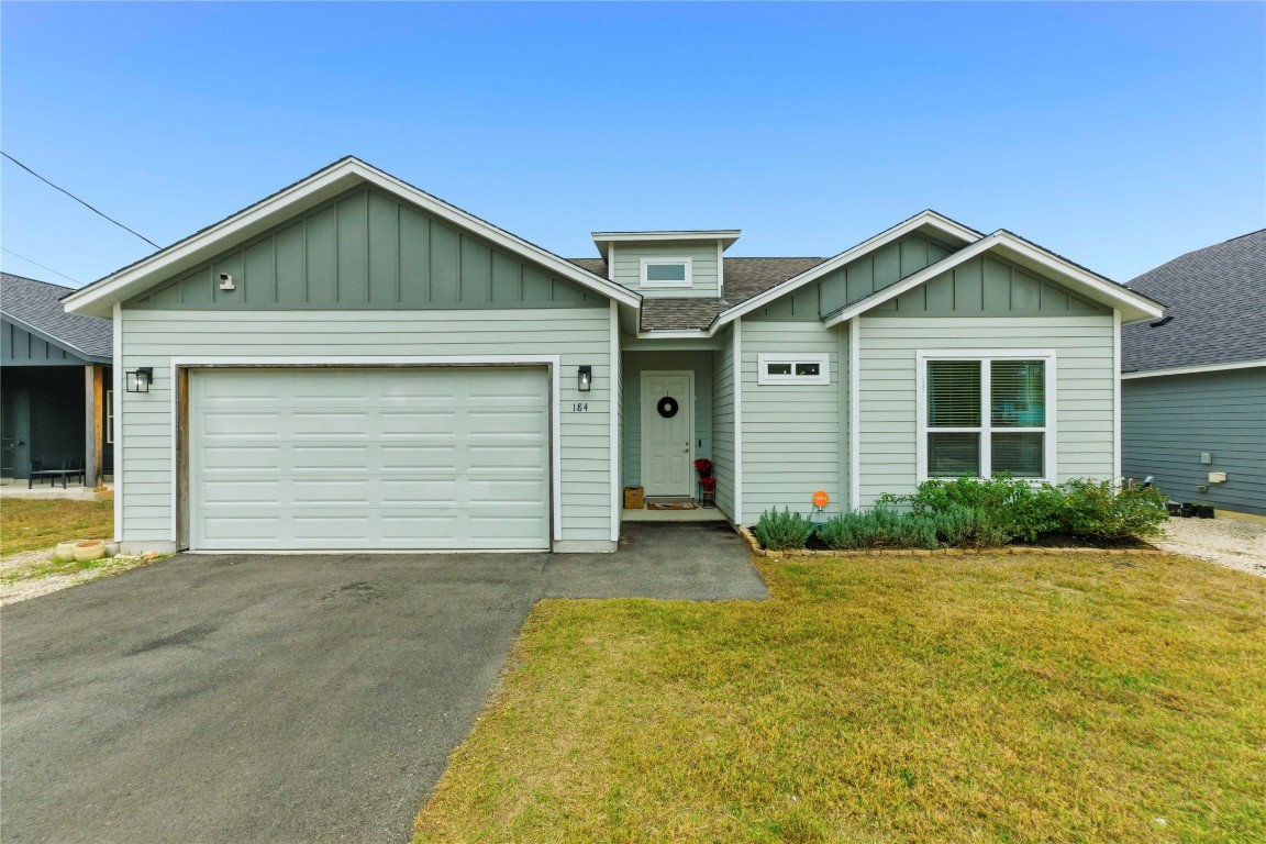 View of front facade featuring board and batten siding, a front lawn, asphalt driveway, an attached garage, and a shingled roof