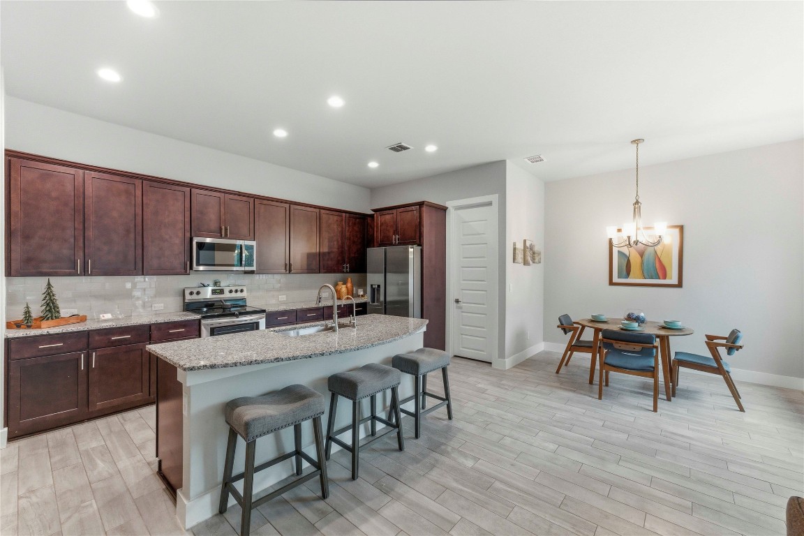 184 Granite Road Spring Branch, TX 78070 - Photo 5 of 27 Kitchen featuring appliances with stainless steel finishes, dark brown cabinetry, light stone countertops, a breakfast bar, and decorative light fixtures