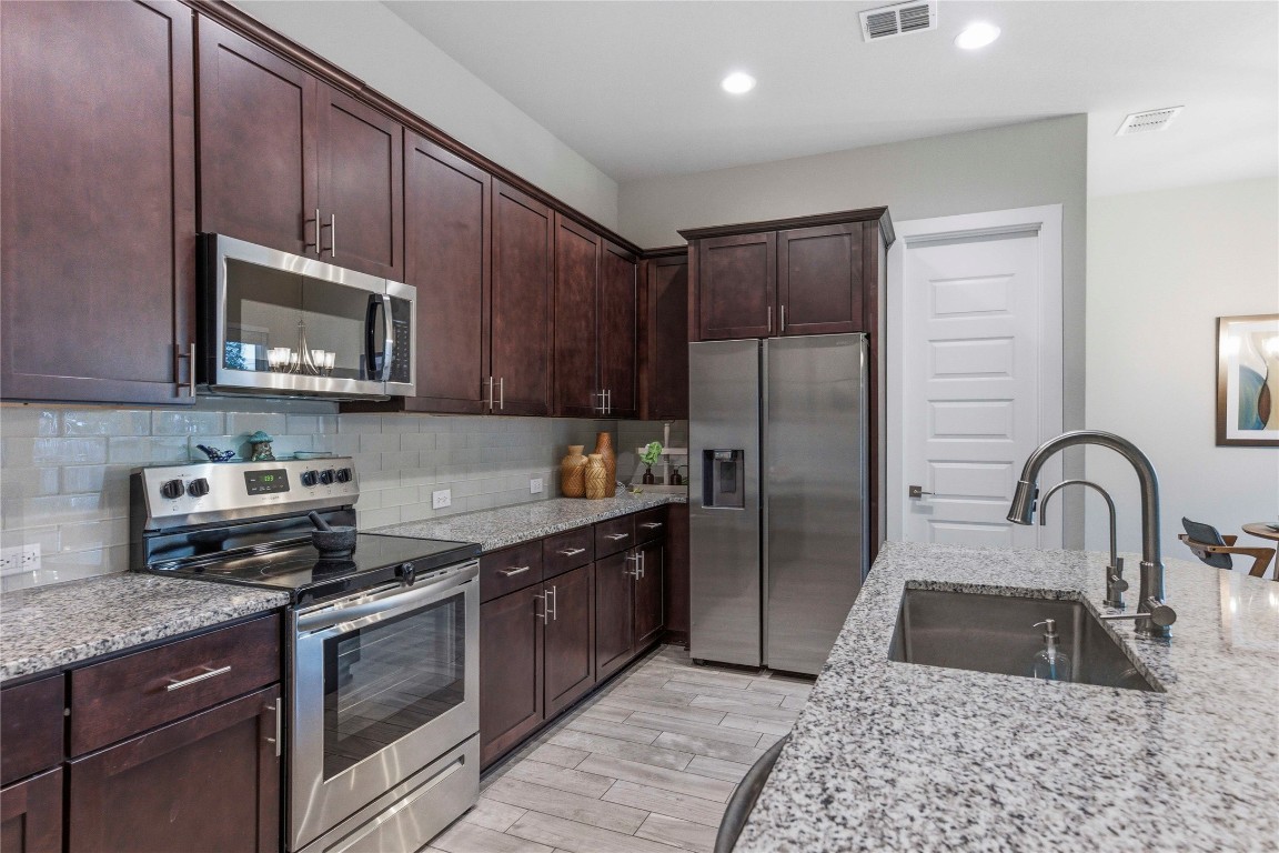 184 Granite Road Spring Branch, TX 78070 - Photo 7 of 27 Kitchen featuring stainless steel appliances, light stone counters, wood tiled floors, dark brown cabinets, and decorative backsplash
