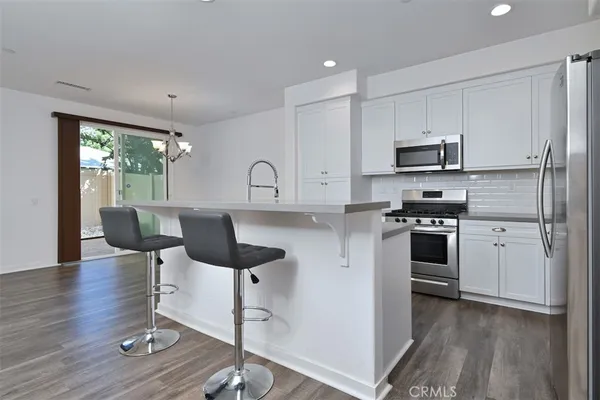 a kitchen with stainless steel appliances a stove a sink a refrigerator white cabinets and wooden floor