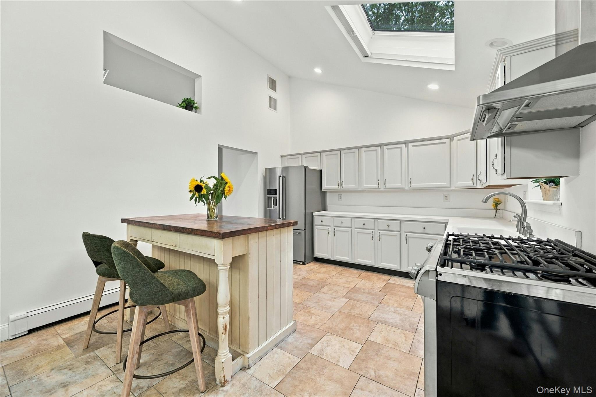 16 Georgann Road Manorville, NY 11949 - Photo 11 of 32 Vaulted ceilings with a skylight, white cabinetry, stainless steel appliances, a center island with a wood-finish countertop, and tile flooring