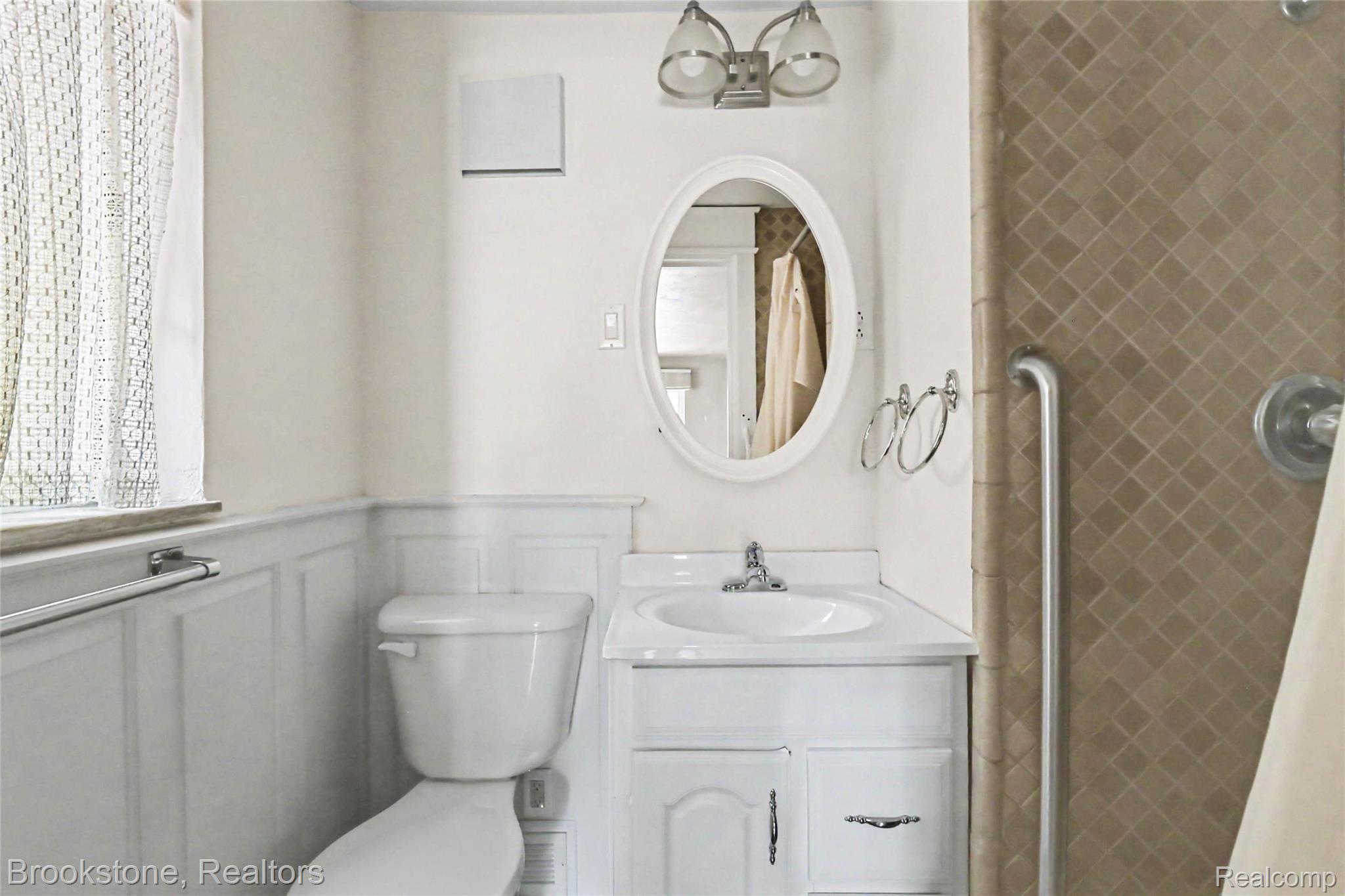 416 East Maple Street Mason, MI 48854 - Photo 10 of 18 Bathroom featuring wainscoting, an oval mirror, a white vanity with integrated sink, and diamond-patterned shower tiling
