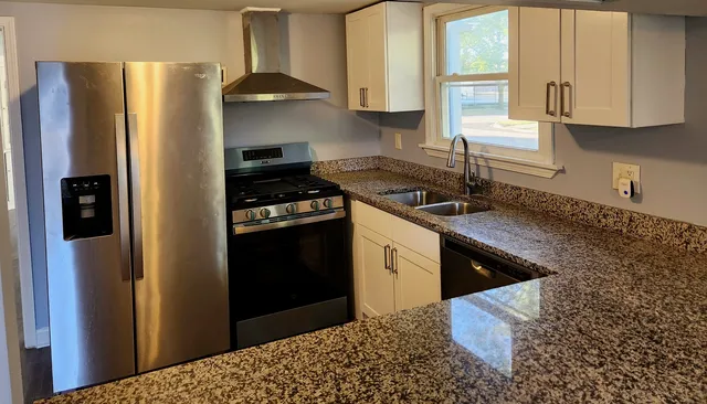 a kitchen with stainless steel appliances granite countertop a refrigerator a sink a stove and white cabinets