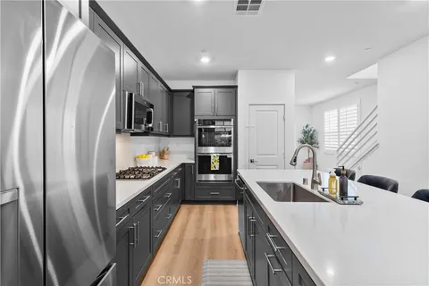 a kitchen with stainless steel appliances granite countertop a refrigerator a sink dishwasher a stove and a dining table with wooden floor