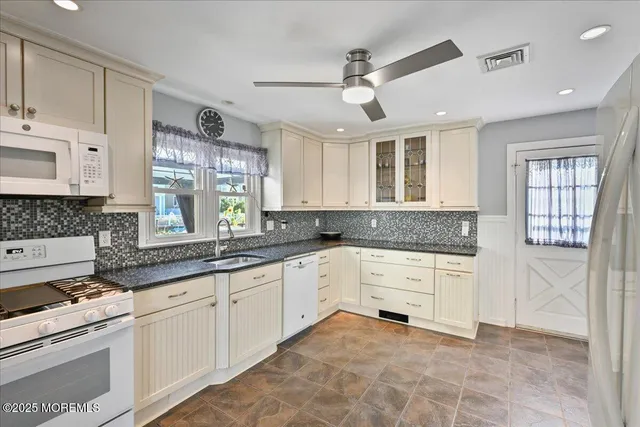 a kitchen with granite countertop white cabinets white appliances a sink and a window