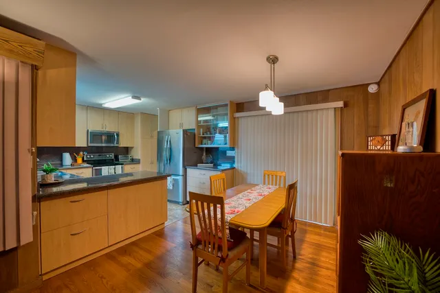 a kitchen with stainless steel appliances granite countertop a refrigerator a sink dishwasher a dining table and chairs with wooden floor