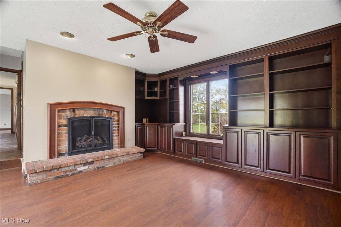 11710 Butternut Road Chardon, OH 44024 - Photo 18 of 48 Unfurnished family room featuring a fireplace, ceiling fan, dark wood-style floors, a textured ceiling, and built in shelves