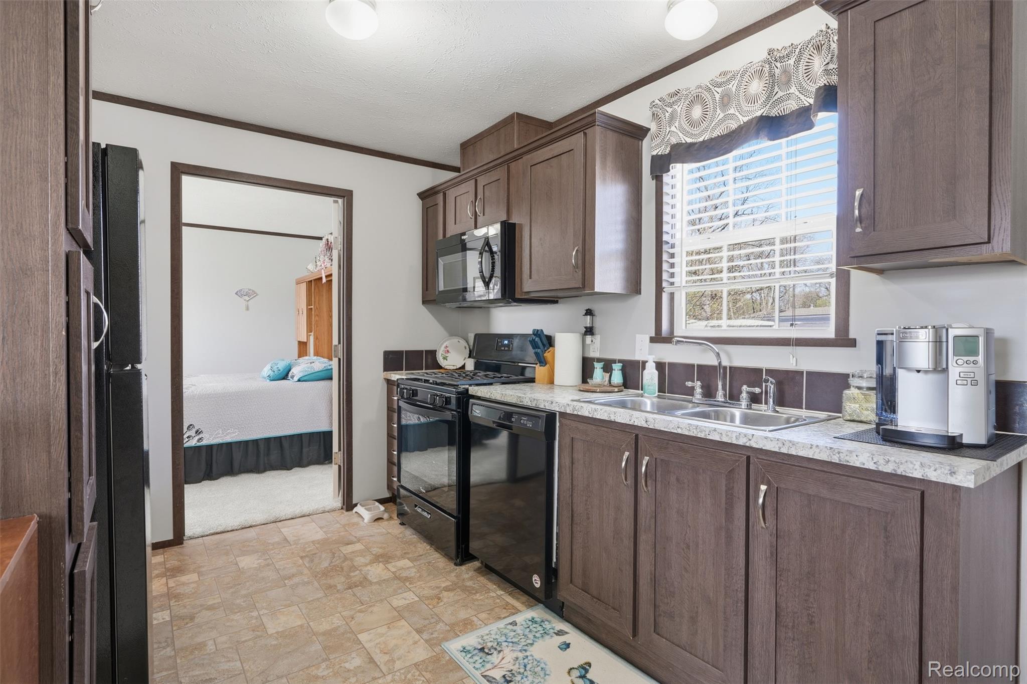 440 Flamingo Street Rochester, MI 48309 - Photo 14 of 32 Kitchen with black appliances, light countertops, stone finish floors, dark wood finish cabinetry, and ornamental molding