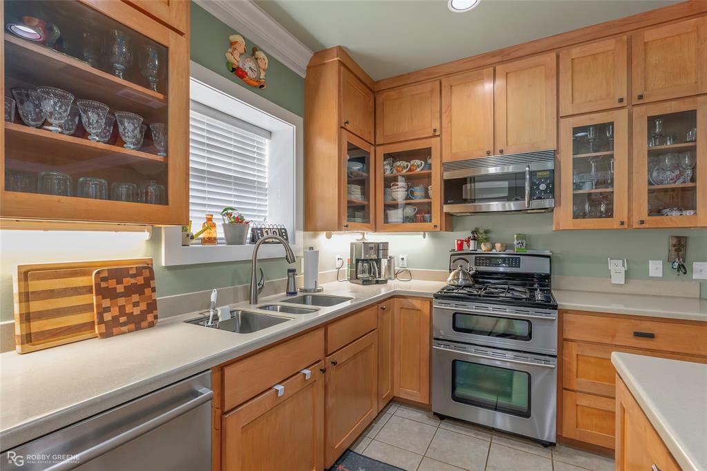 6340 Pine Hill Road Shreveport, LA 71107 - Photo 18 of 40 Kitchen featuring stainless steel appliances, glass insert cabinets, light countertops, light tile patterned floors, and crown molding