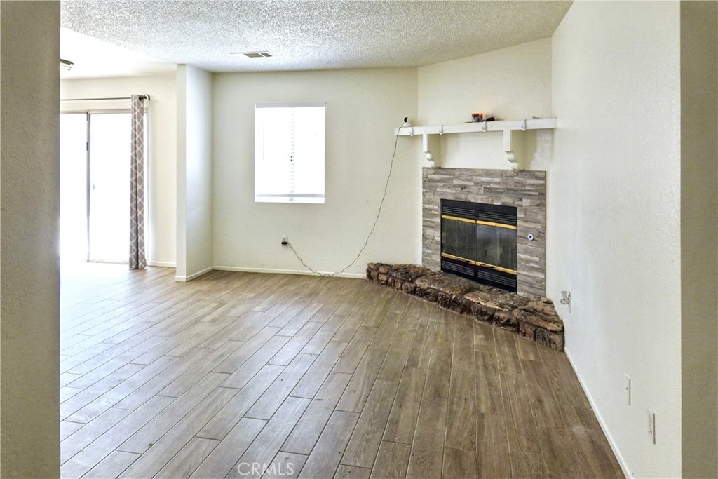 10403 Buckboard Circle Adelanto, CA 92301 - Photo 5 of 20 an empty room with wooden floor a fireplace and windows