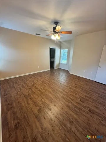 an empty room with wooden floor chandelier fan and windows