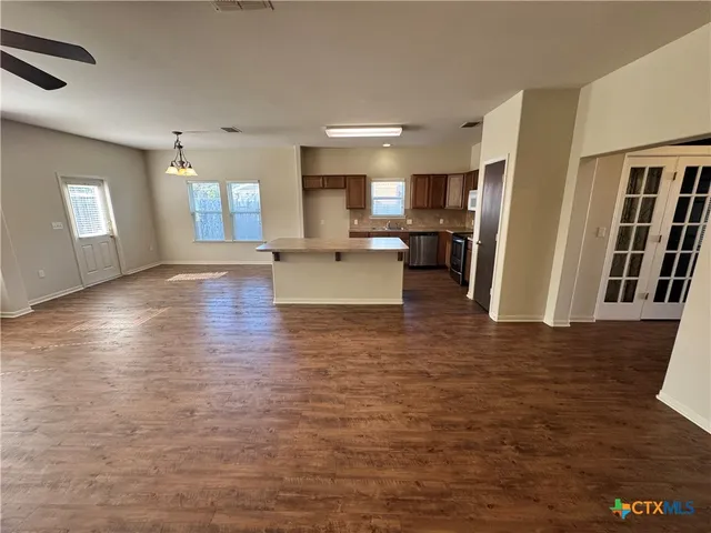 a view of a living room with kitchen island stainless steel appliances wooden floor and window