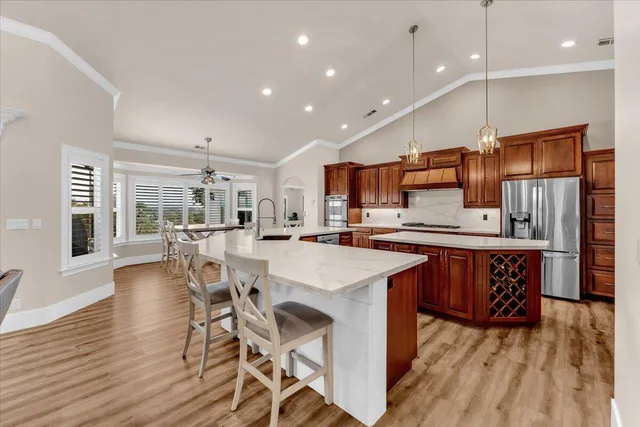 a kitchen with stainless steel appliances kitchen island granite countertop a refrigerator a stove top oven a sink dishwasher and white cabinets with wooden floor