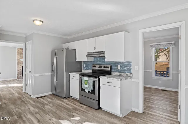 a kitchen with stainless steel appliances granite countertop a stove top oven a refrigerator and white cabinets with wooden floor