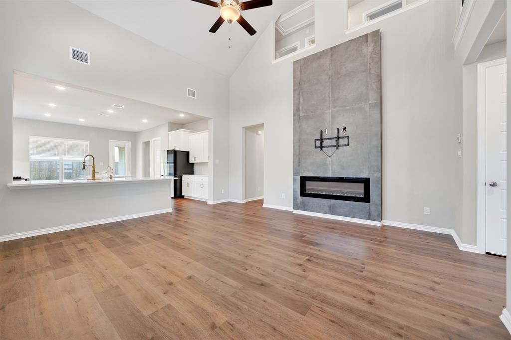 3506 Riley Street Fate, TX 75087 - Photo 8 of 32 Soaring vaulted ceiling, LVP flooring, linear electric fireplace with floor-to-ceiling surround, high transom windows, and an open concept kitchen with a breakfast bar