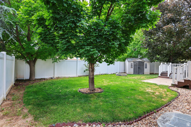 142 East 2675th Street South Clearfield, UT 84015 - Photo 37 of 49 Fenced backyard featuring mature shade trees, a well-maintained lawn, a built-in fire pit, and a storage shed
