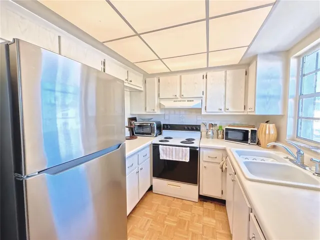 a kitchen with stainless steel appliances granite countertop a refrigerator a sink dishwasher a stove with white cabinets and wooden floor