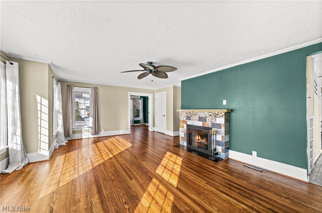 4609 Middle Ridge Road Perry, OH 44081 - Photo 5 of 27 Unfurnished living room with hardwood / wood-style flooring, a ceiling fan, a glass covered fireplace, a textured ceiling, and crown molding