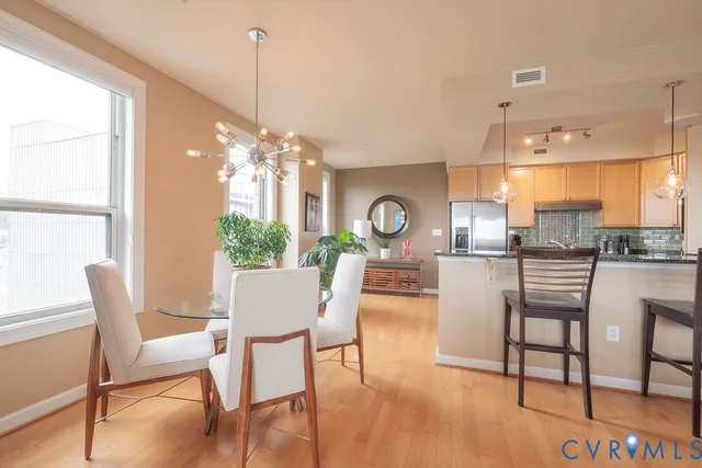 a view of a kitchen with kitchen island stainless steel appliances a refrigerator a stove a sink a dining table and chairs with wooden floor