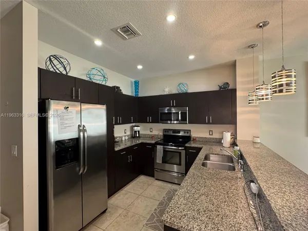 a kitchen with stainless steel appliances granite countertop a refrigerator a sink a stove a microwave and island