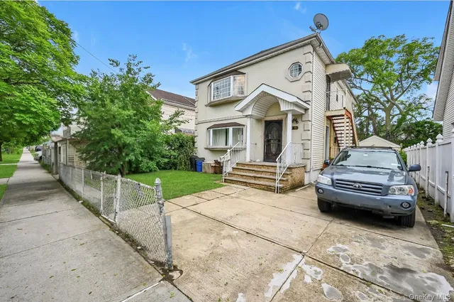 a view of a white house with a small yard and large trees