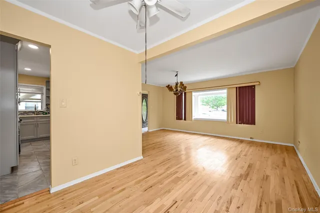 an empty room with wooden floor chandelier fan and windows