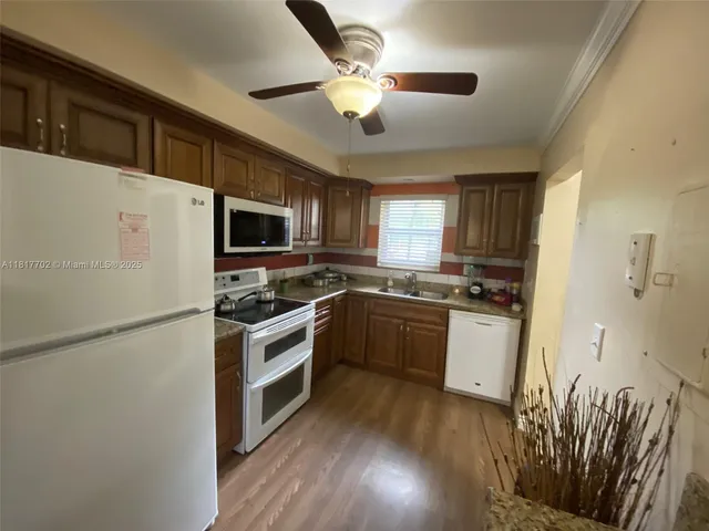 a kitchen with granite countertop a refrigerator a stove top oven a sink and wooden floor