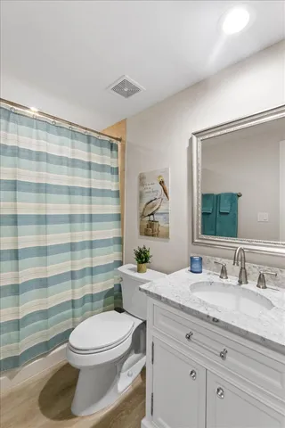 a bathroom with a granite countertop toilet a sink a mirror and shower curtain
