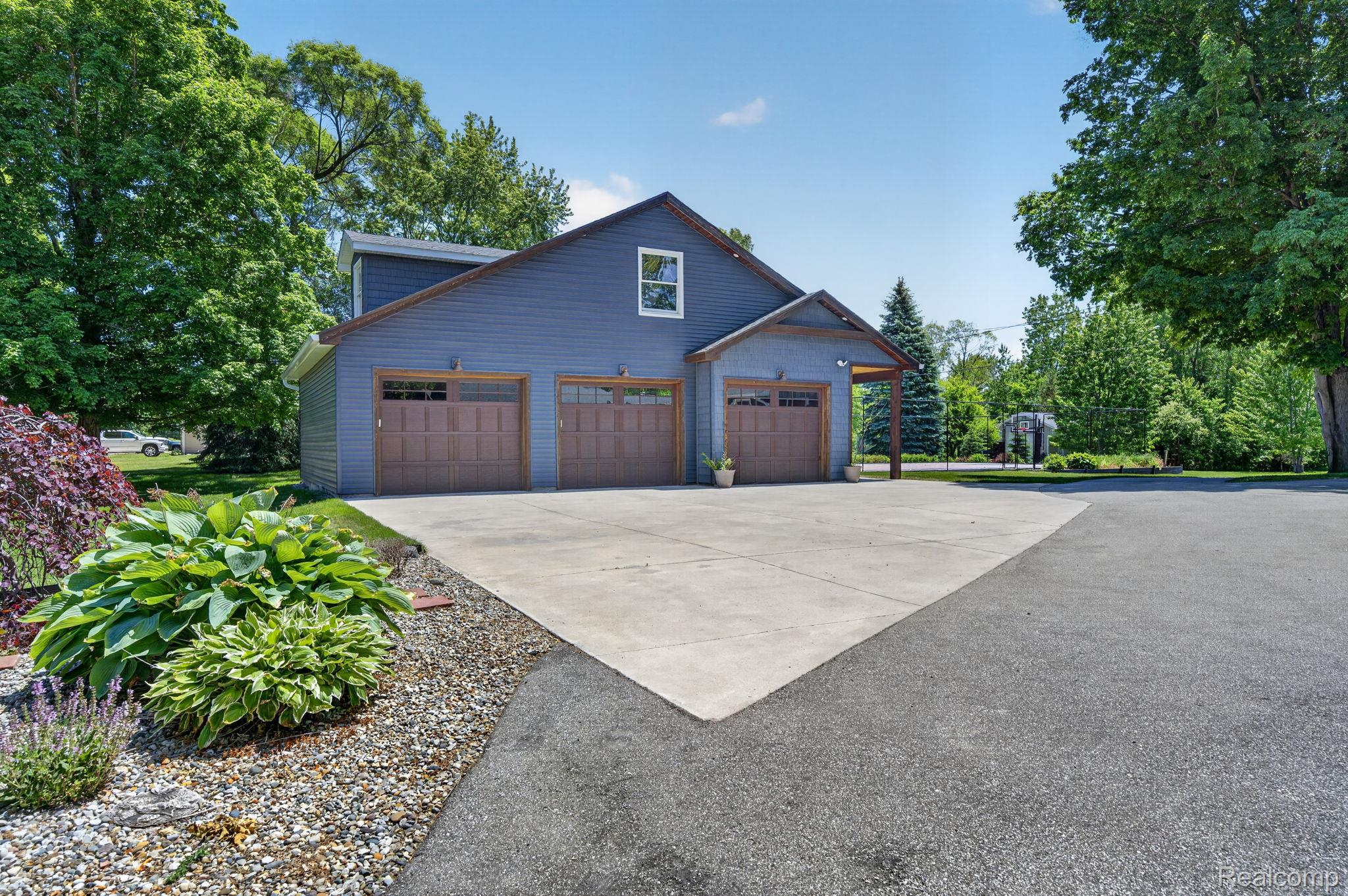 9353 Hill Road Swartz Creek, MI 48473 - Photo 8 of 98 Spacious three-car garage with wood-finish doors and a covered entry, featuring blue siding and a concrete driveway