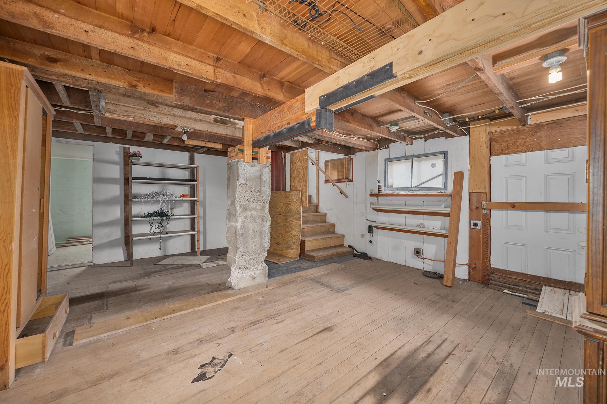 61 Southwest 4th Street Ontario, OR 97914 - Photo 38 of 42 Exposed wood beam ceiling in a lower-level space featuring a concrete support pillar, unpainted wood flooring, built-in shelving, and a small window