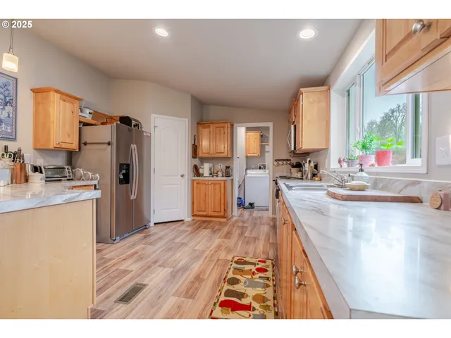 a kitchen with stainless steel appliances granite countertop a refrigerator a sink dishwasher a stove and white countertops with wooden floor