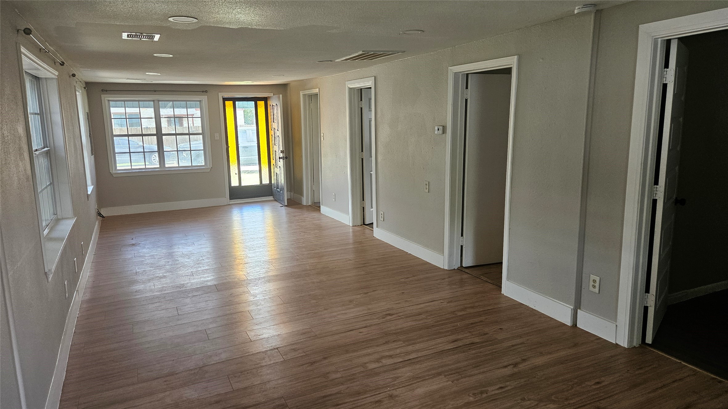 2415 Perry Street Baytown, TX 77521 - Photo 3 of 23 This photo showcases a bright, open living room with vinyl plank floors, neutral walls, and multiple windows allowing natural light. It features access to adjacent rooms, perfect for a cozy and inviting living space.
