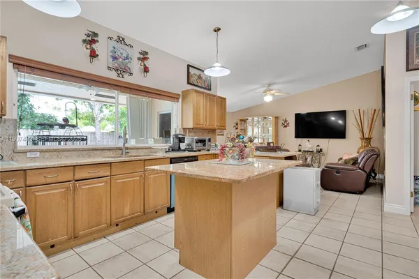a kitchen with stainless steel appliances kitchen island granite countertop a sink and a flat screen tv