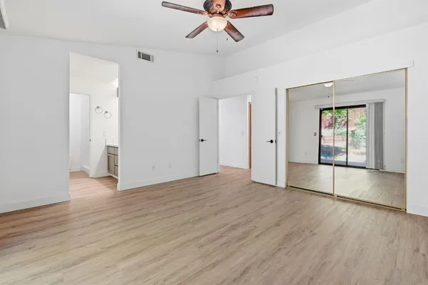 an empty room with wooden floor a ceiling fan and windows