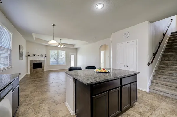 a view of an empty room and kitchen with fireplace ceiling fan