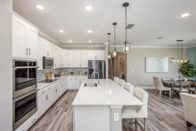 a kitchen with stainless steel appliances kitchen island granite countertop a stove a sink a refrigerator and a dining table with wooden floor