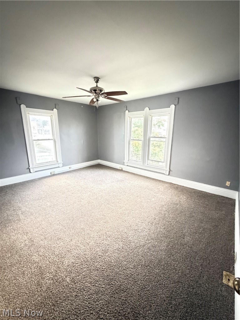 Spacious room featuring neutral carpeting, two large windows with decorative trim, and a ceiling fan
