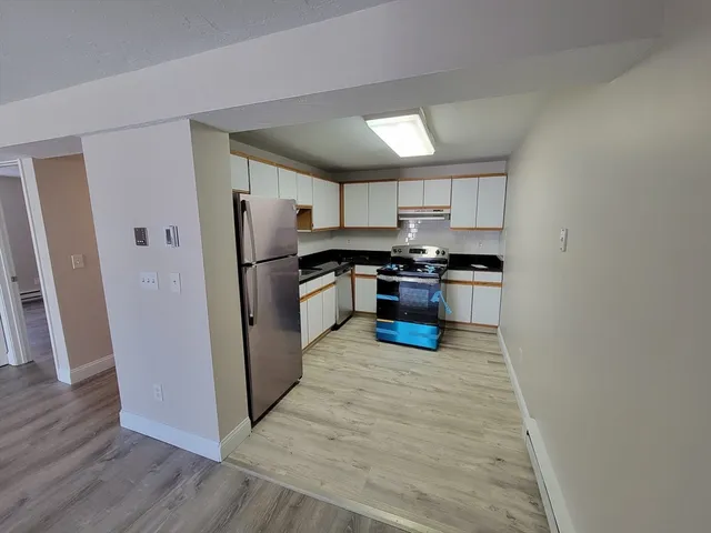 a kitchen with stainless steel appliances granite countertop white cabinets a refrigerator a sink a stove a microwave and wooden floors