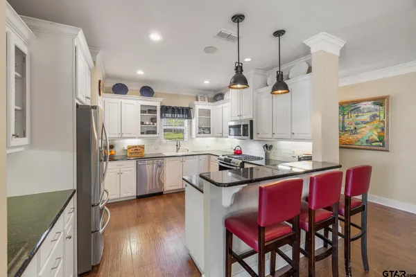 a kitchen with stainless steel appliances kitchen island granite countertop a sink a stove a refrigerator dining table and chairs
