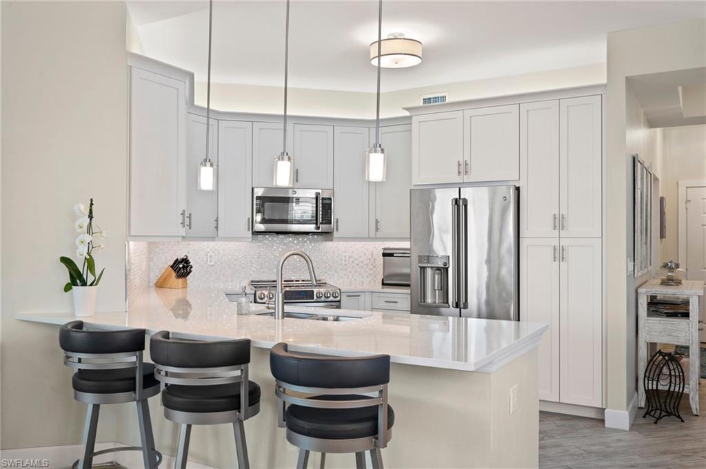450 Launch Circle, Unit 201 Naples, FL 34108 - Photo 3 of 43 a kitchen with stainless steel appliances a table chairs refrigerator and microwave