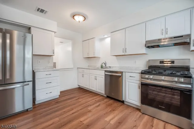a kitchen with white cabinets stainless steel appliances and wooden floor