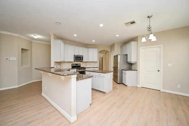 a kitchen with stainless steel appliances kitchen island granite countertop a stove top oven a refrigerator a sink and white cabinets with wooden floor