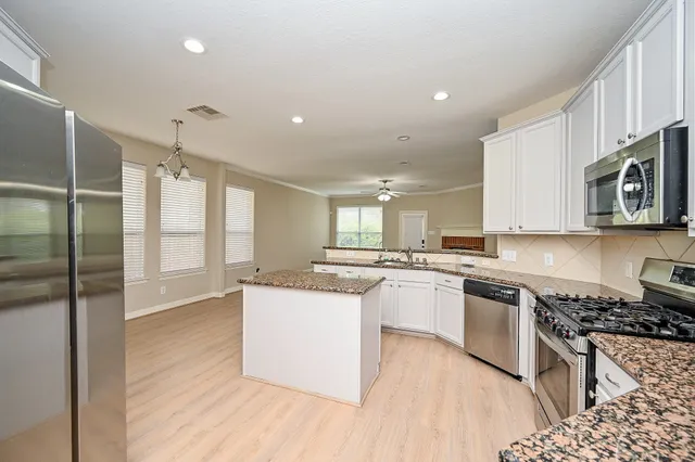 a kitchen with stainless steel appliances granite countertop a stove top oven a sink dishwasher a refrigerator and white cabinets with wooden floor
