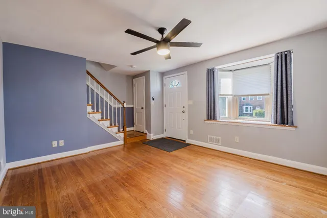 a view of an empty room with wooden floor and a ceiling fan