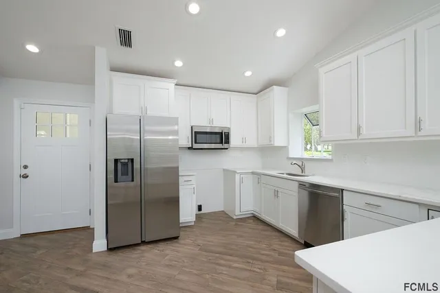 a kitchen with stainless steel appliances granite countertop a refrigerator a sink a stove a microwave and white cabinets